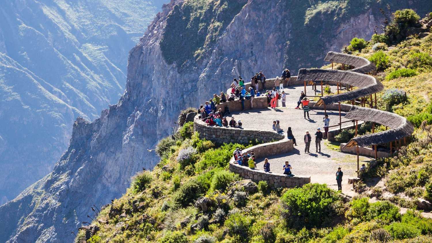Viewpoint at Colca Canyon in southern Peru, with visitors observing the dramatic cliffs and deep valley from a curved stone terrace – cultural tourism and nature observation in the Andes.