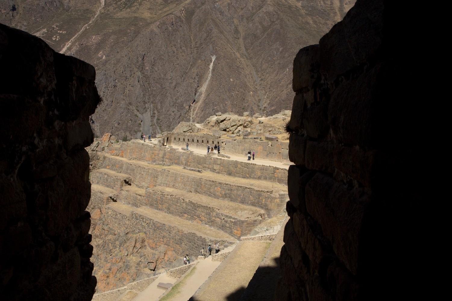 Vista de las terrazas de piedra de la Fortaleza de Ollantaytambo en el Valle Sagrado de Perú, enmarcadas por los muros de una antigua puerta inca, ejemplo de ingeniería defensiva y agrícola.