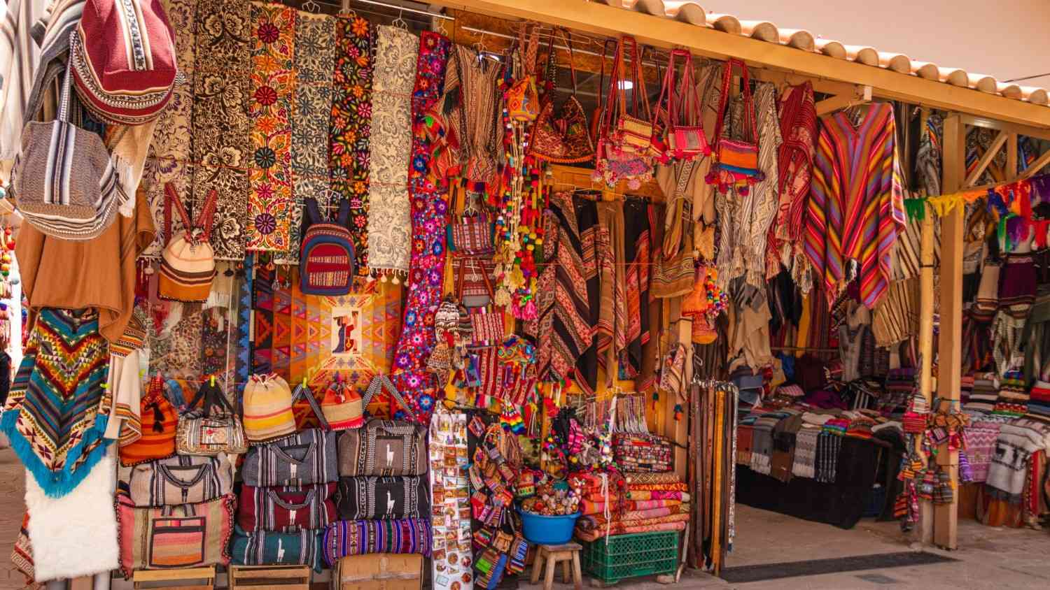 Colorful handicrafts and textiles at Pisac Market in the Sacred Valley, Peru – vibrant Andean ponchos, bags, and woven patterns for sale.