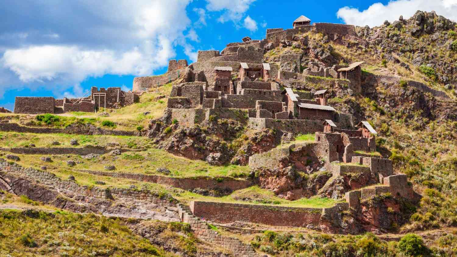 Inca ruins of Pisac archaeological site in the Sacred Valley, Peru – ancient stone terraces and hillside structures under a blue sky.
