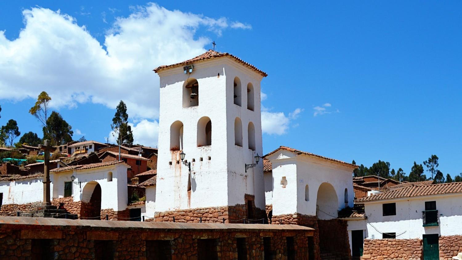 Colonial church tower in Chinchero, Sacred Valley, Peru – whitewashed walls, red-tiled roof, and stone base under a clear blue sky.