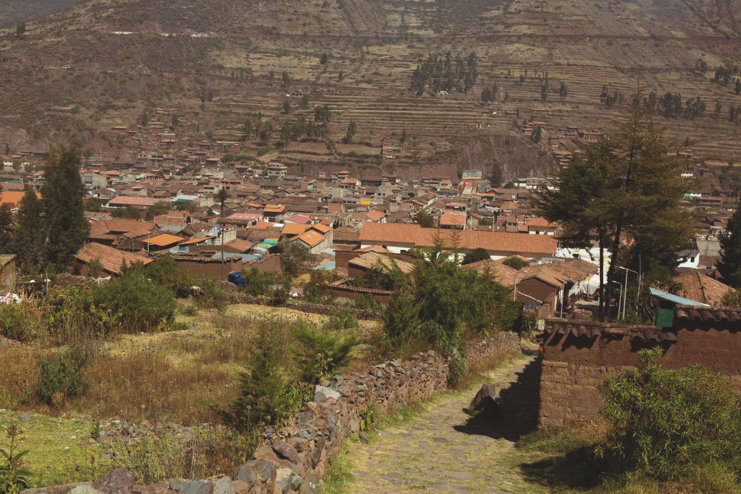 Panoramic view of Ollantaytambo Village in the Sacred Valley of the Incas, with traditional adobe houses, cobblestone streets, and surrounding agricultural terraces – a cultural tourism and trekking hub in the Peruvian Andes.