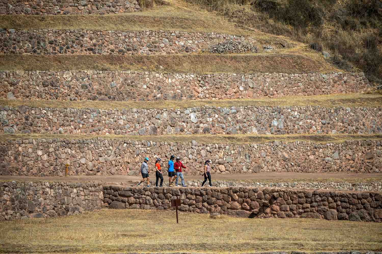 Group of visitors walking alongside the stone terraces at the Pisac Ruins, one of the archaeological gems of the Sacred Valley of the Incas – cultural tourism and hiking in the Peruvian Andes.