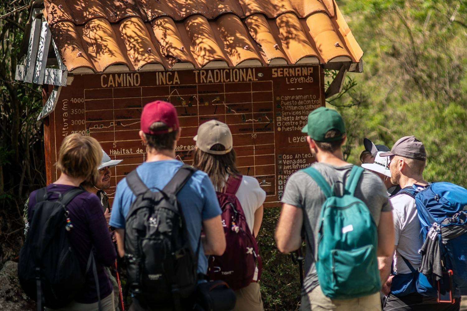 Group of hikers gathered at the Traditional Inca Trail entrance sign, reviewing information before starting their trek to Machu Picchu.