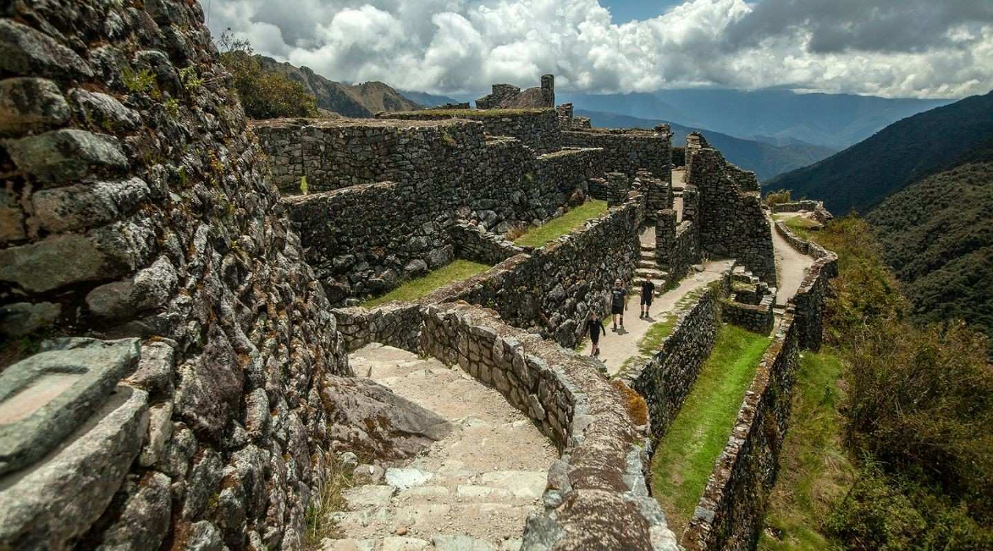 Stone terraces and archaeological ruins along the Inca Trail to Machu Picchu, with hikers walking through the site.