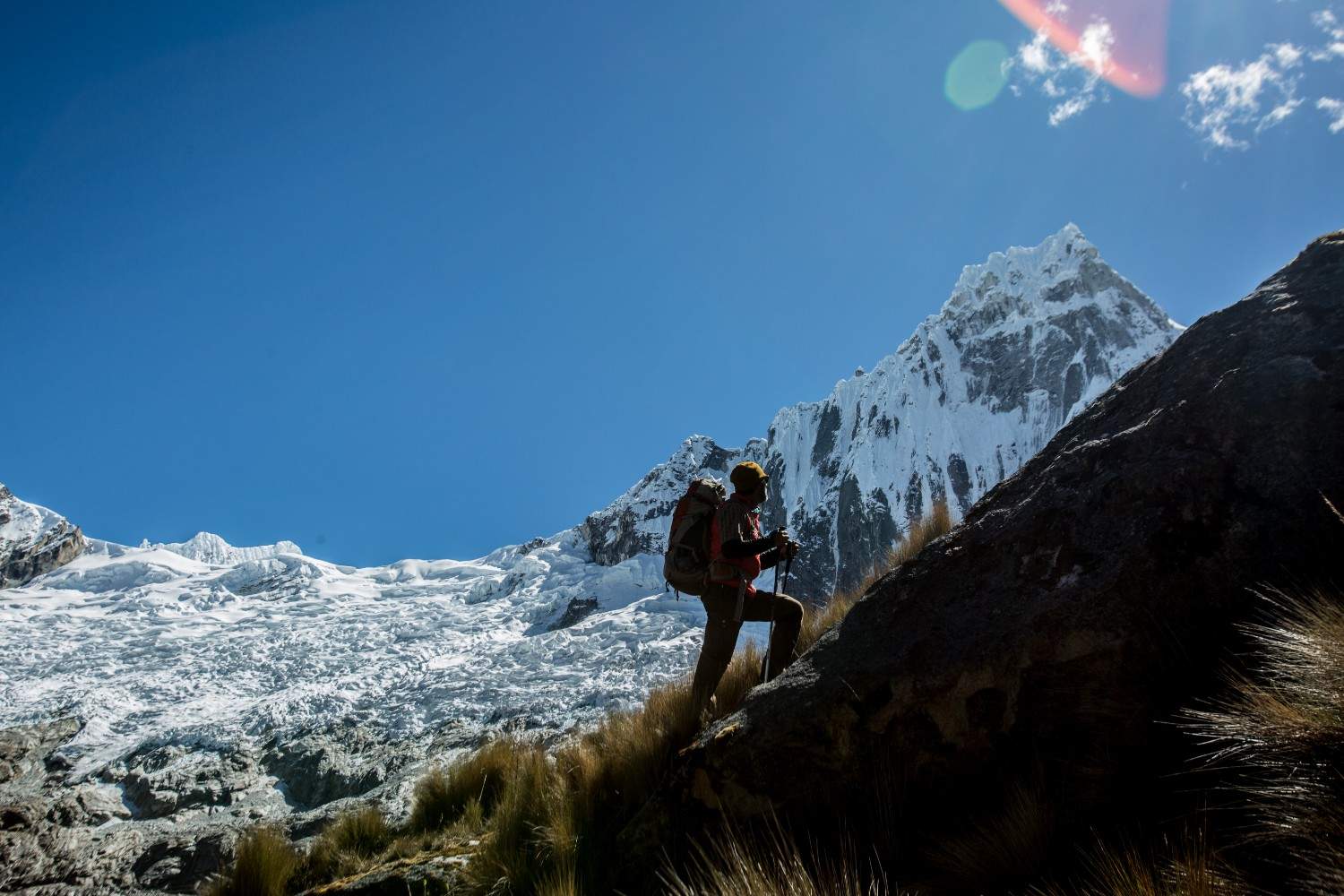 Silueta de un excursionista ascendiendo una pendiente empinada en el Santa Cruz Trek, con picos andinos nevados y glaciares en la Cordillera Blanca bajo un cielo azul despejado.