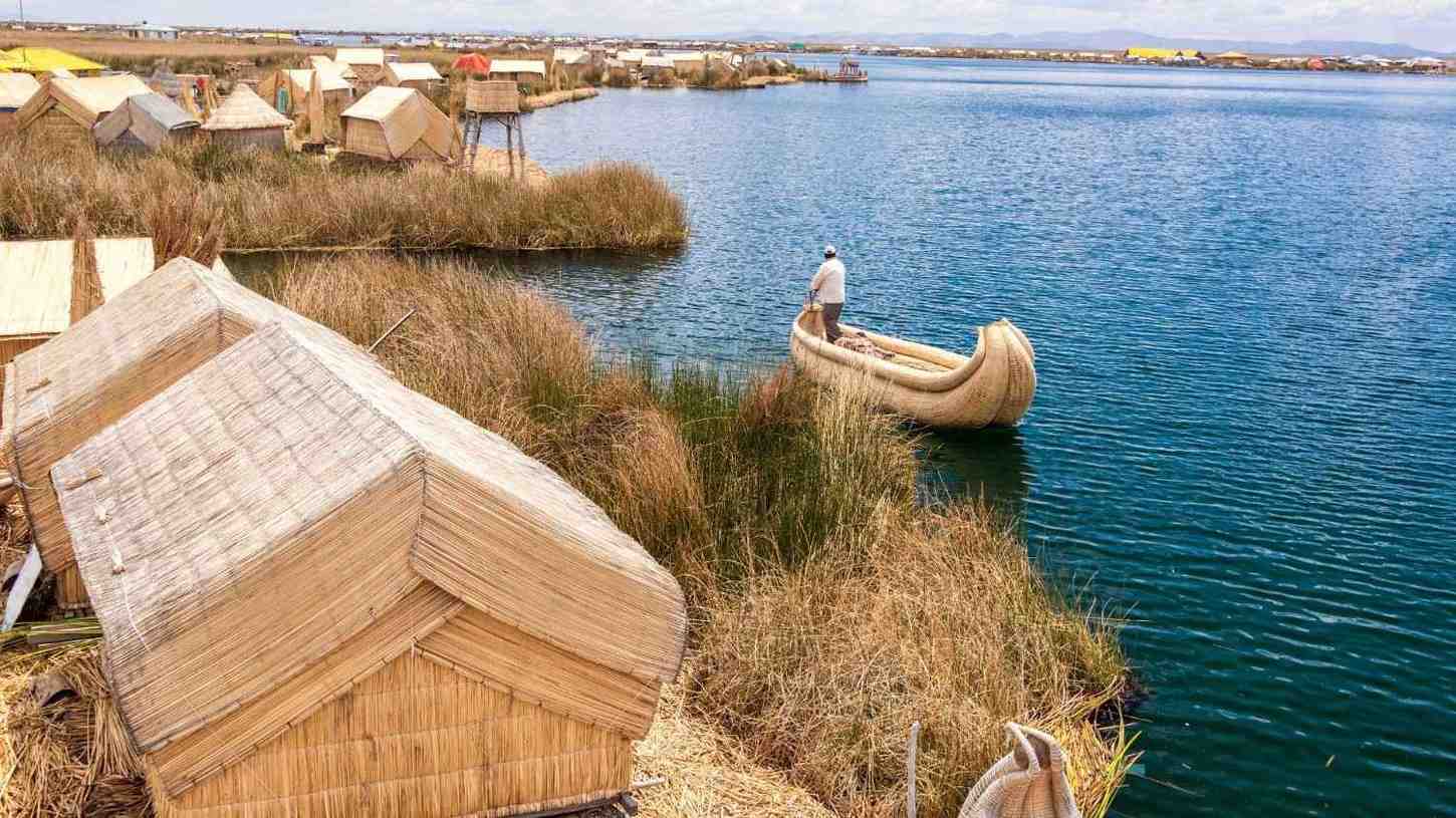 Man sailing a traditional totora reed boat beside the floating houses of the Uros on Lake Titicaca altitude – cultural and experiential tourism in the Andean highlands.