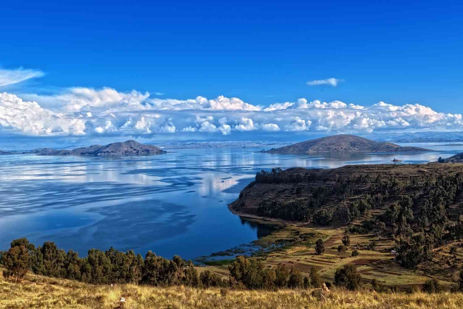 Wide view of Lake Titicaca from the Peruvian shore, with islands and mountains reflected in its blue waters – cultural tourism and nature in the Andean highlands.