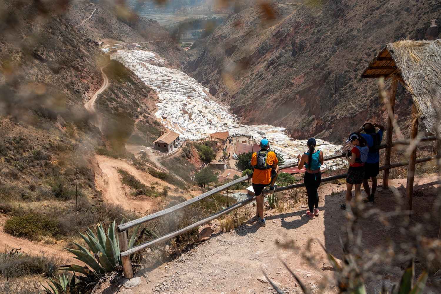 Corredores de trail en el sendero hacia las Salineras de Maras, deteniéndose en un mirador sobre las terrazas blancas de sal talladas en la ladera durante un tour guiado de running y cultura en el Valle Sagrado.