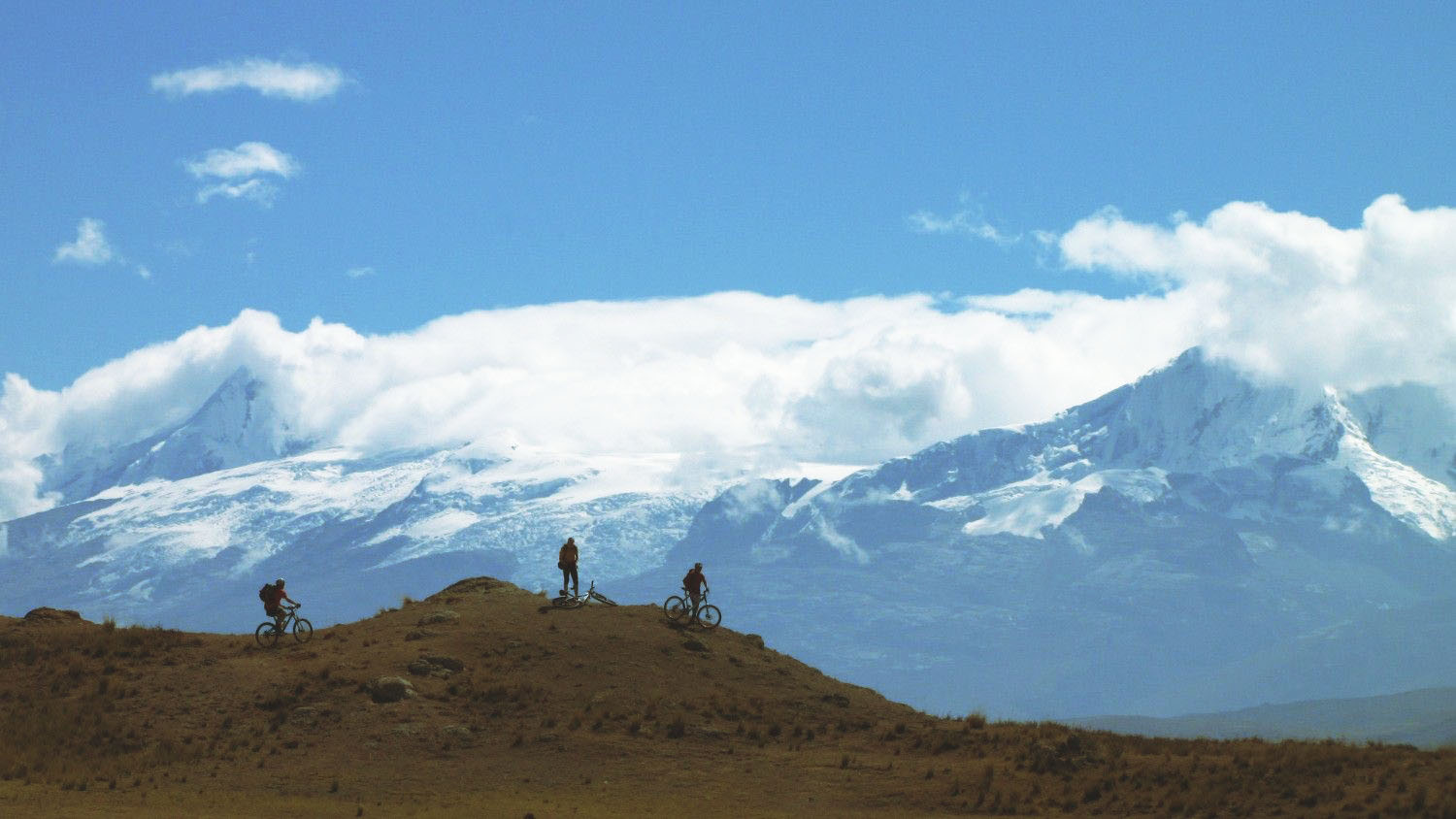 Cyclists riding in the highlands of Huaraz, Peru, with snow-capped peaks of the Cordillera Blanca in the background – outdoor adventure in the Andes.