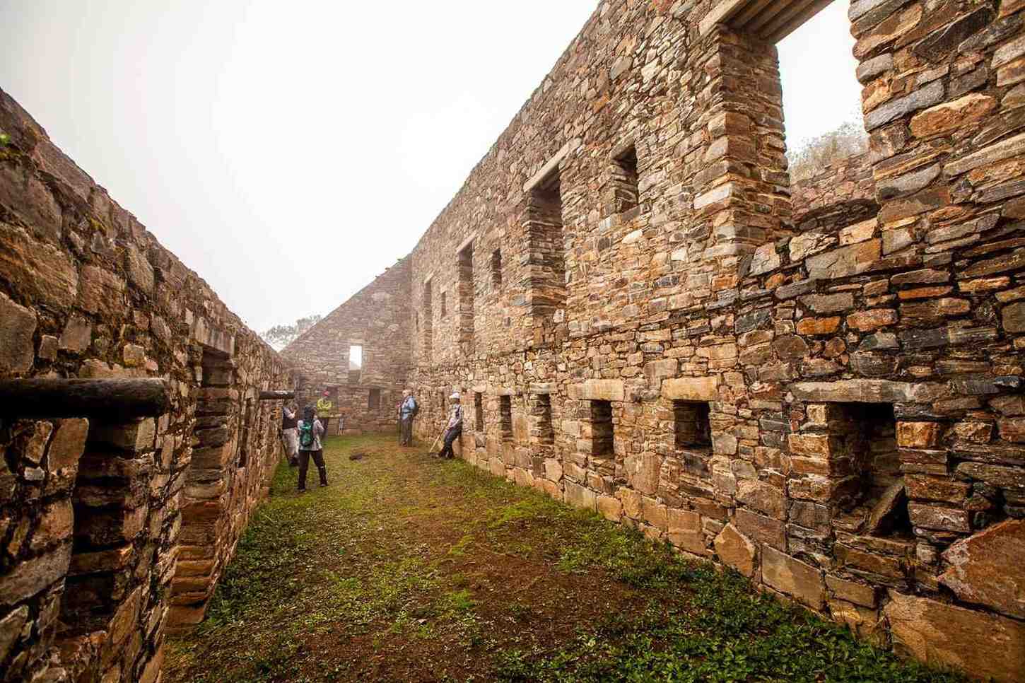 Vista interior de las estructuras de piedra de “Los Galpones” en la plaza principal del sitio arqueológico de Choquequirao, con visitantes explorando los muros incas.