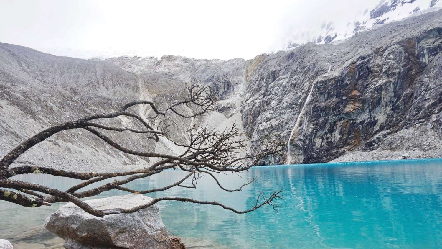 Aguas turquesa de la Laguna 69 con picos rocosos y una pequeña cascada en el Parque Nacional Huascarán, Perú.